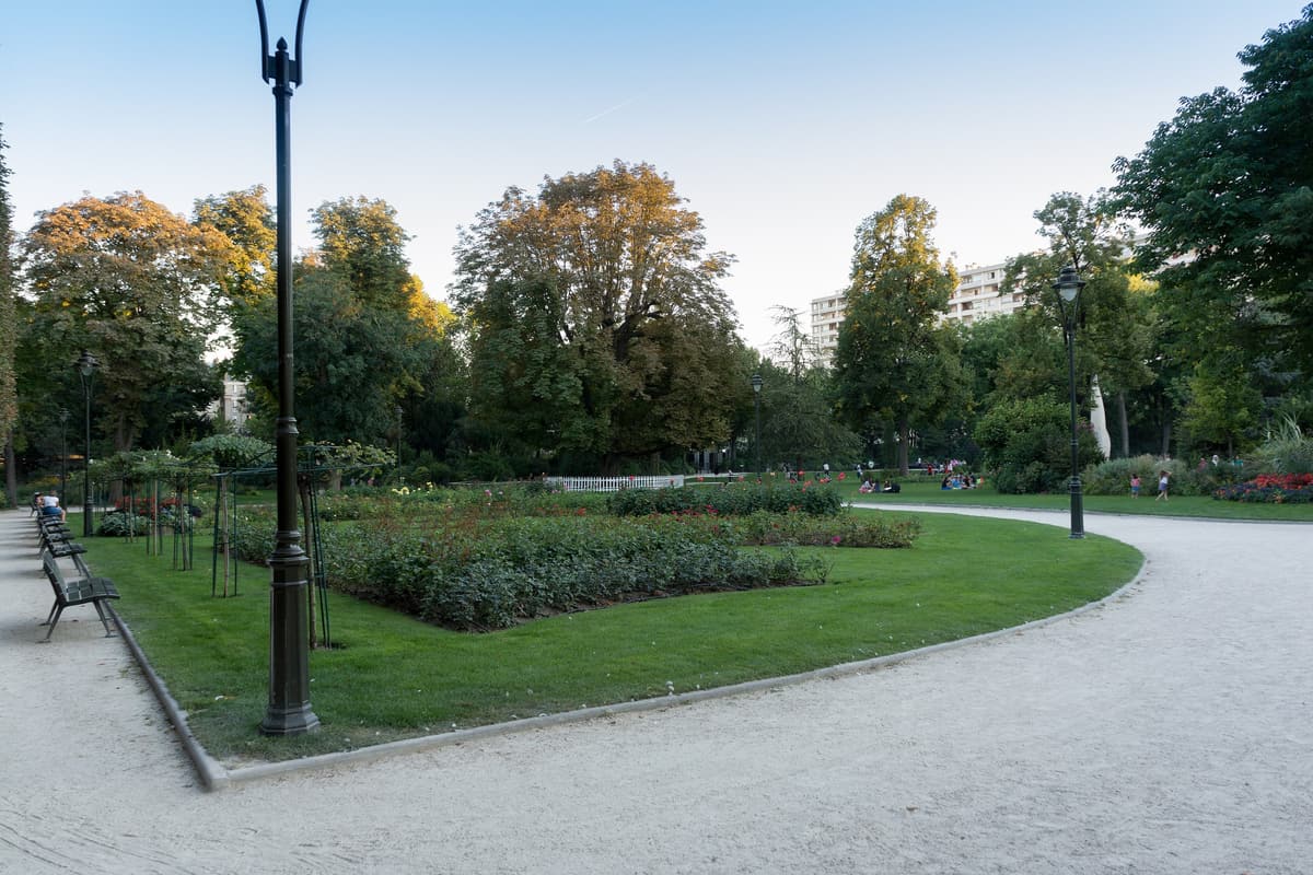 Allées et pelouses du parc de la Planchette, massifs de rosiers et grands arbres, un lampadaire au premier plan.